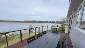 A deck with a table and chairs overlooking a lake, a grill, and a view of the water. - Luxury Waterfront Home Private Dock, Stunning Views & Sleeps 14 (South Kingstown)