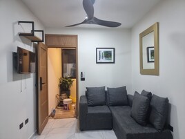 Una sala de estar moderna con un sofá gris, un ventilador de techo, un televisor montado y un cuadro enmarcado en la pared.