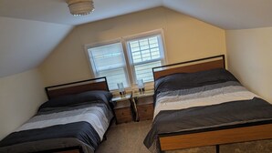 A bedroom with two single beds, a nightstand, a lamp, and a window with blinds.