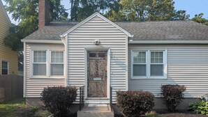 A single-story house with a front door, two windows on the left, and a small porch area.