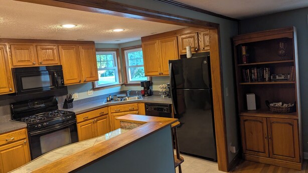 A kitchen with wooden cabinets, a black refrigerator, a microwave, and a stove.