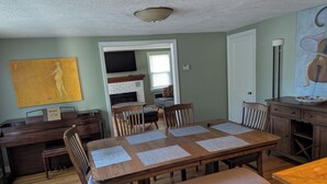 A dining area with a wooden table, four chairs, and a bench. There is a fireplace, a television, and a painting on the wall.