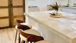 A modern kitchen with a large island, bar stools, and a ceiling fan. - Casa Verde - 180° Ocean Views Rooftop Deck - King Beds (VIEQUES)