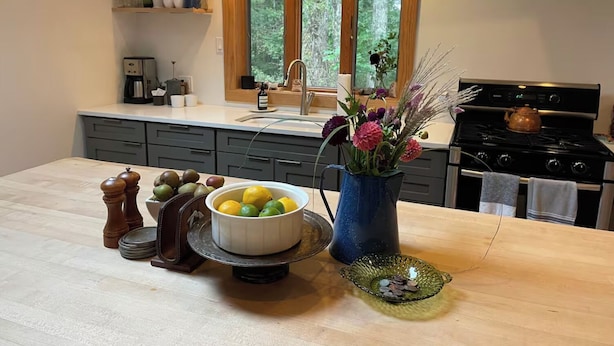 A kitchen with a wooden countertop, a sink, a stove, and a window with a view of trees.
