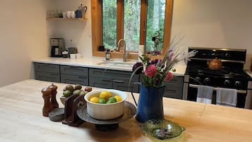Une cuisine avec un plan de travail en bois, un évier, une cuisinière et une fenêtre donnant sur des arbres.