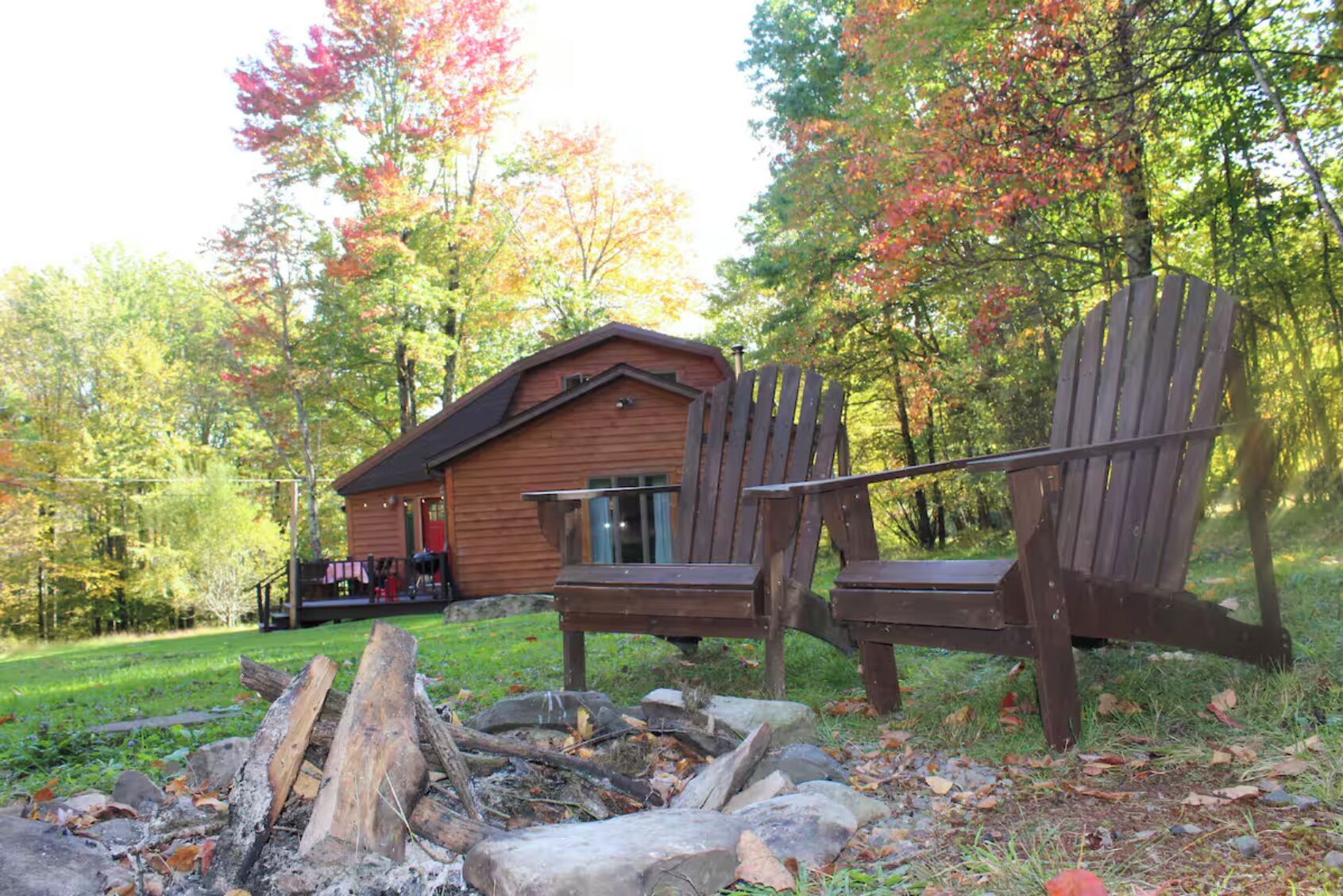 Une cabane avec un foyer et deux fauteuils Adirondack en bois.
