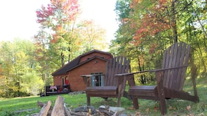 A cabin with a fire pit and two wooden Adirondack chairs.