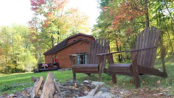 Une cabane avec un foyer et deux fauteuils Adirondack en bois.
