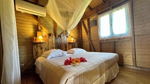A wooden cabin room with a bed, bedside lamps, and a window. - Gîte Santa Maria (Grand-Bourg)