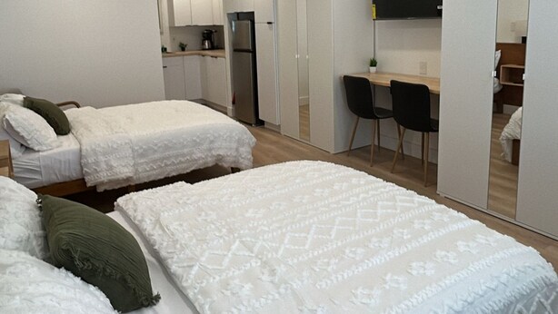 Quarto de hotel moderno com duas camas, uma escrivaninha, uma cadeira, uma televisão e uma kitchenette.