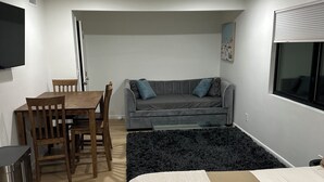 A bedroom with a bed, a gray sofa, a wooden dining table with chairs, a black rug, and a ceiling fan. -  Deluxe Guest Suite with Private Entrance, Near San Diego Beaches, Sleeps 4 (San Diego)