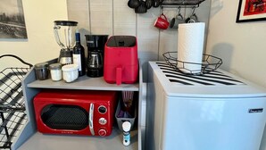 A compact kitchen with a red toaster, a white microwave, a red coffee maker, a blender, and a coffee machine. There are utensils hanging on the wall and a basket with a roll of paper towels.