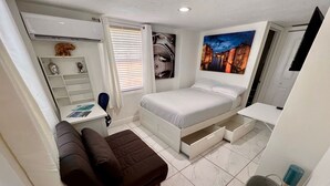 A compact bedroom with a bed, a small desk, a sofa, and a storage unit.