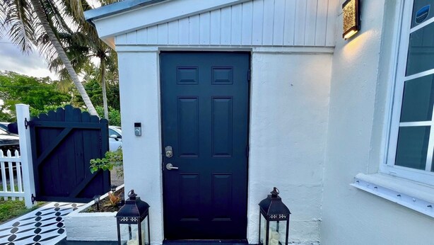A black door with a welcome mat, two lanterns, and a patterned floor.