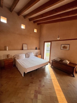 A bedroom with a large bed, wooden beams, a dresser, and a bench.