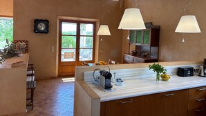 A kitchen with a large island, wooden cabinets, pendant lights, a clock, and a view through the door. - Country House 'Son Gener' with Private Pool, Private Terrace and Wi-Fi (Son Servera)