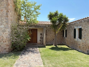 A stone building with a wooden door, a small window with shutters, and a palm tree.