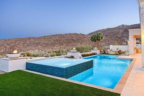 Ein Swimmingpool mit Bergblick, umgeben von einer gepflegten Rasenfläche und einer Sitzgelegenheit im Freien.
