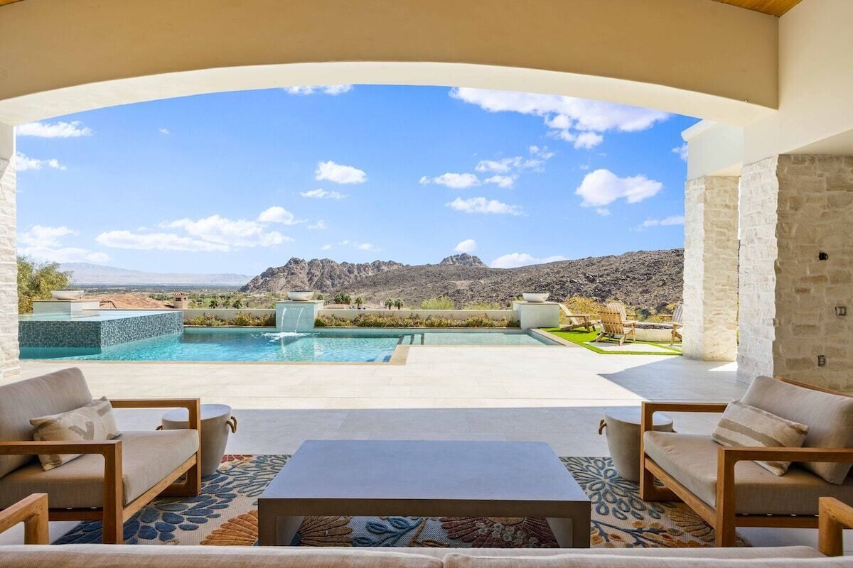 A pool area with a view of mountains, outdoor seating, and a stone wall.