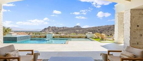 A pool area with a view of mountains, outdoor seating, and a stone wall.