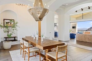 A spacious dining area with a wooden table and chairs, a large woven chandelier, and a view of the outdoors. - Poolside Oasis, Golf Paradise, Hot Tub, Spa, Views (La Quinta)
