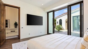 A bedroom with a large bed, a flat-screen TV mounted on the wall, and a sliding glass door leading to an outdoor area. - Poolside Oasis, Golf Paradise, Hot Tub, Spa, Views (La Quinta)