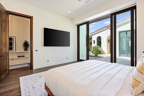 A bedroom with a large bed, a flat-screen TV mounted on the wall, and a sliding glass door leading to an outdoor area. - Poolside Oasis, Golf Paradise, Hot Tub, Spa, Views (La Quinta)