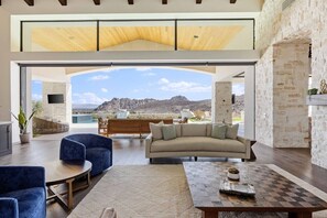 A spacious living area with a large window, a sofa, a coffee table, and a view of a mountainous landscape.