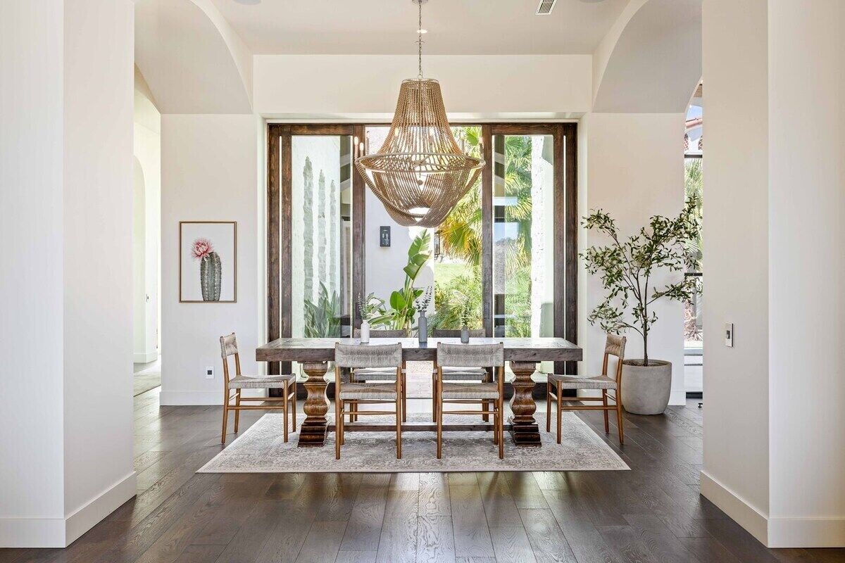 Un comedor con una larga mesa de madera, seis sillas, una lámpara colgante de fibras tejidas y un ventanal con vistas a zonas verdes.