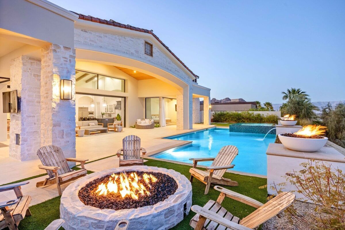 Una casa moderna con piscina, mobiliario de exterior y una chimenea.
