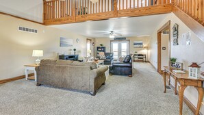 A spacious living room with a high ceiling, a wooden staircase, and a view of the backyard.