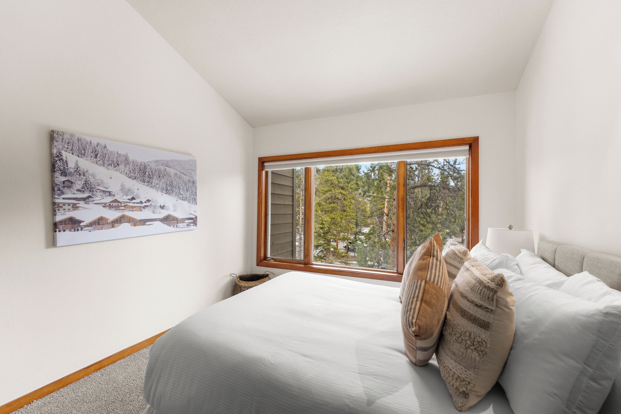 Een slaapkamer met een groot raam, een bed met wit beddengoed, en een schilderij van een besneeerd landschap.