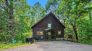 A log cabin with a porch, a bench, and a sign indicating its location. - Private Smoky Mtn Cabin | Hot Tub + 3 Fireplaces (Sevierville)