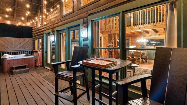 Interior de una cabaña de madera con jacuzzi, comedor y ventanas amplias.