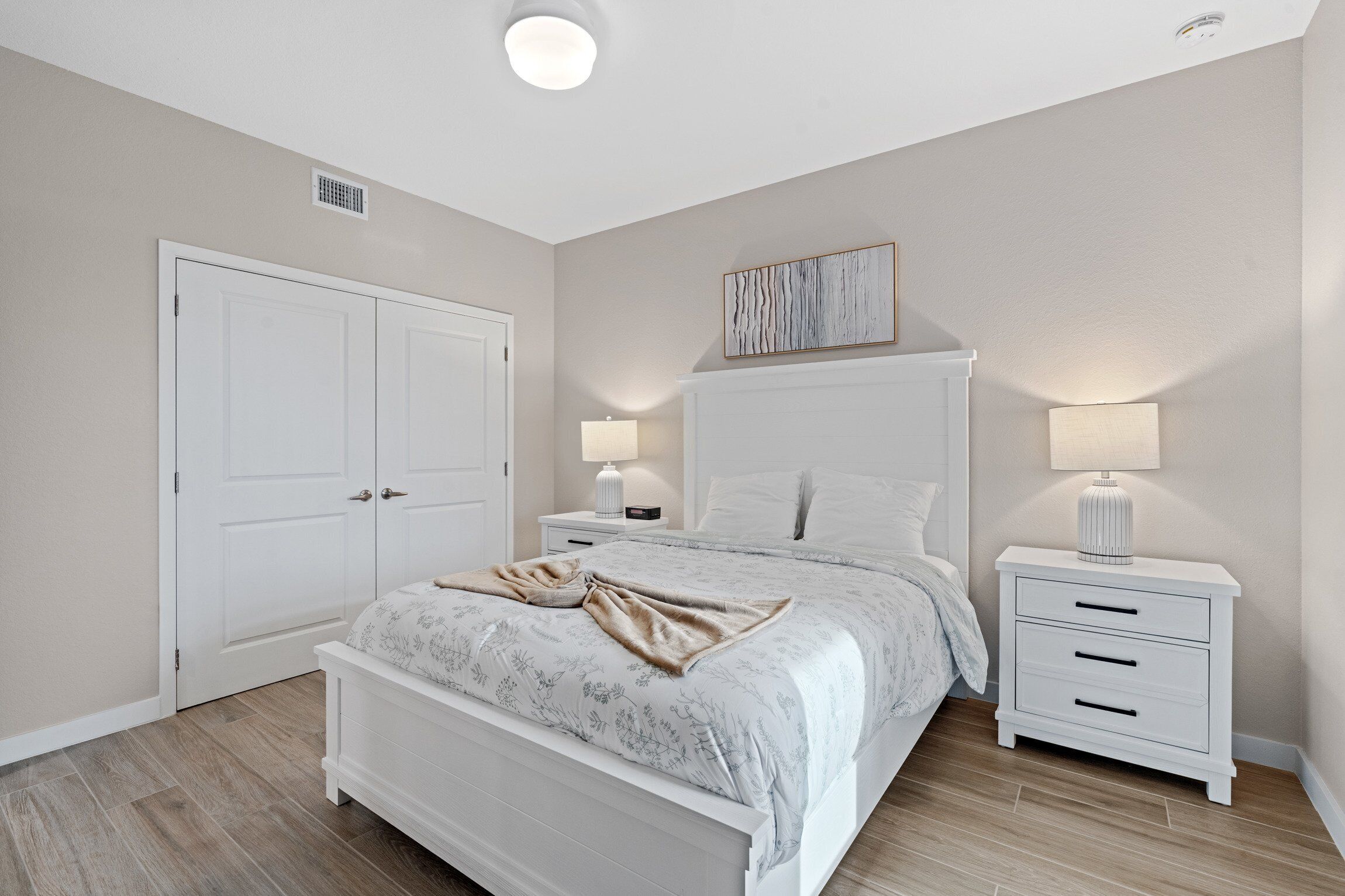 A bedroom with a bed, nightstands, a wall-mounted artwork, and a door.
