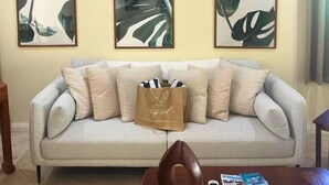 A living room with a light grey sofa, multiple cushions, a brown bag on the sofa, and three framed abstract paintings on the wall.