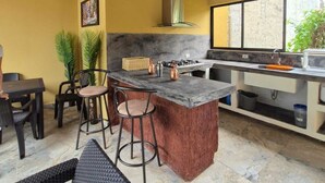 Une cuisine dotée d’un îlot central, de tabourets de bar, d’un coin repas avec des chaises et d’un plafond recouvert de chaume.