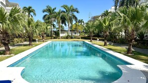 A rectangular swimming pool with a white edge, surrounded by palm trees and a well-maintained lawn. - Apartment in a residence facing the sea (Las Terrenas)
