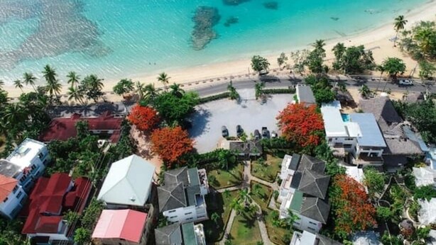 An aerial view of a coastal area with a beach, clear blue water, and buildings with red roofs. - Apartment in a residence facing the sea (Las Terrenas)