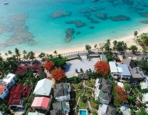 An aerial view of a coastal area with a beach, clear blue water, and buildings with red roofs. - Apartment in a residence facing the sea (Las Terrenas)