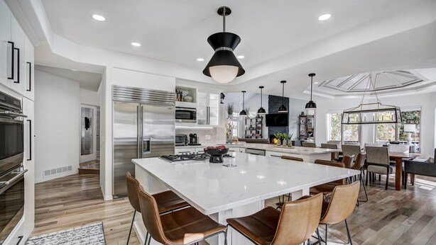 A modern kitchen with a central island, stainless steel appliances, and a dining area with bar stools. - Lakeshore Lodge | Private Hot Tub, Movie Room, & Views for Family Gatherings! (Blue River)