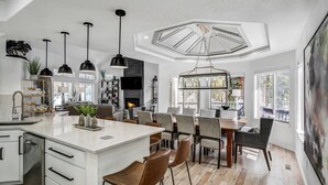A spacious kitchen with a large island, modern pendant lighting, and a view of the outdoors. - Lakeshore Lodge | Private Hot Tub, Movie Room, & Views for Family Gatherings! (Blue River)