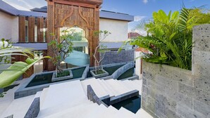 A modern outdoor pool area with a decorative wooden archway, stone steps, and lush greenery.