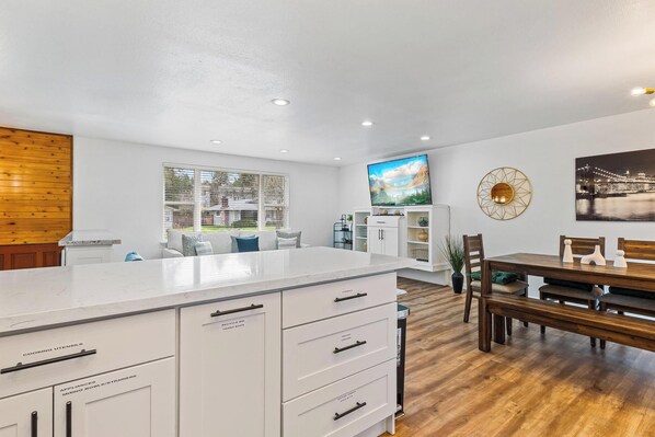 A modern kitchen with white cabinetry, a large island, and a dining area with wooden furniture.