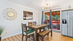 Un comedor con mesa y sillas de madera, una lámpara moderna y un refrigerador.