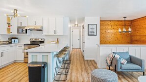 Cocina moderna con armarios blancos, una isla central con taburetes, horno de acero inoxidable y microondas.