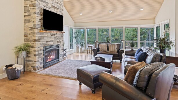 A spacious living room with a stone fireplace, leather sofas, and large windows offering a view of the outdoors. - 20 Aspen - Elegant & Updated & Perfect for Family! SHARC, Hot Tub (Bend)