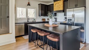 Una cocina moderna con gabinetes oscuros, electrodomésticos de acero inoxidable y una isla central con taburetes de bar.