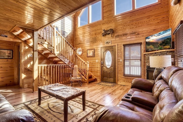 Interior acogedor de una cabaña con paredes de madera, una chimenea, un sofá de cuero y una escalera que lleva a un nivel superior.