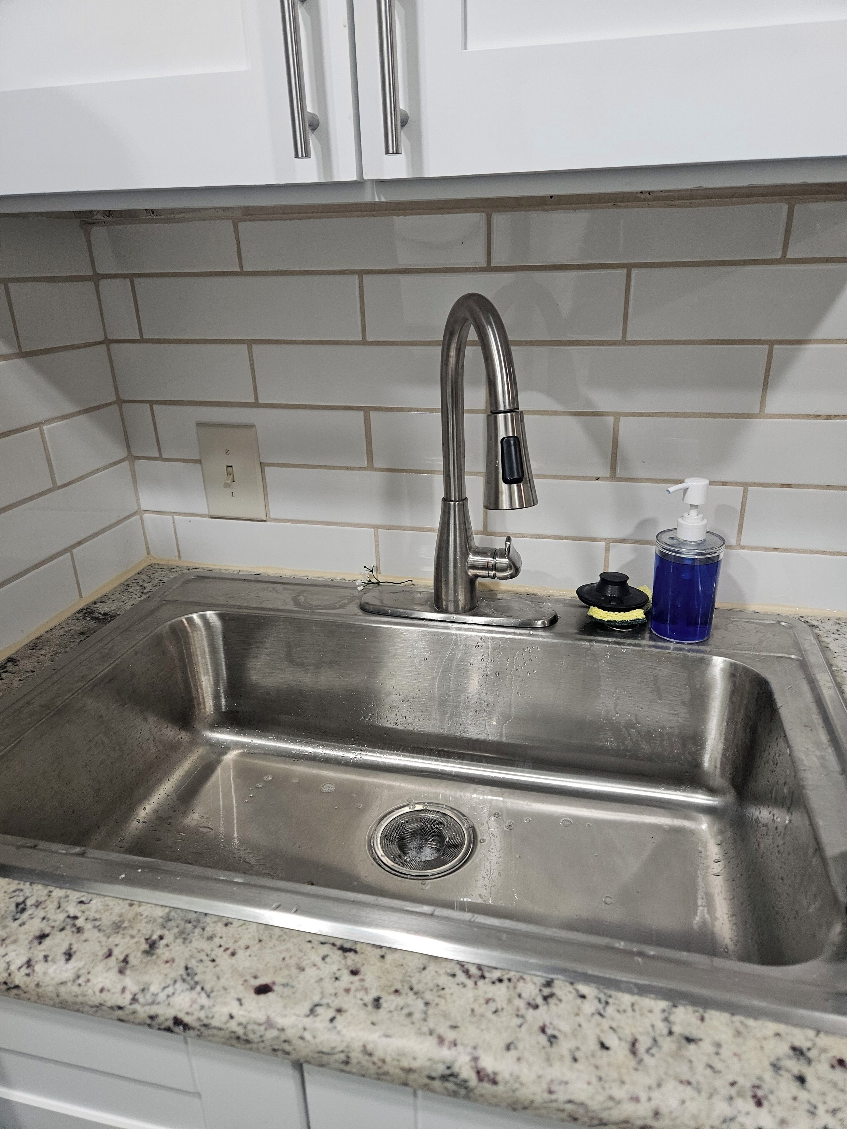 Ein Spülbecken aus Edelstahl mit modernem Wasserhahn, Seifenspender und Abfluss.